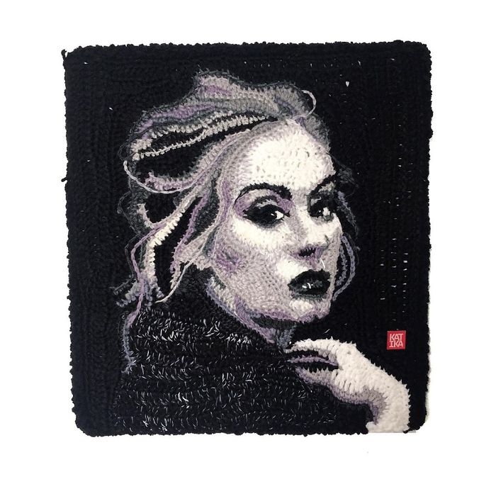 Crochet artist’s detailed portrait of a woman with light hair and dark clothing on a black crocheted background.