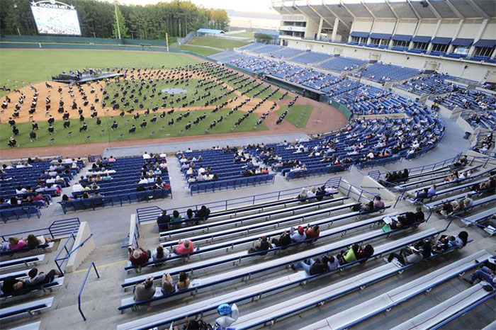 Seniors Sit On A Baseball Field During A Socially Distanced Graduation Ceremony