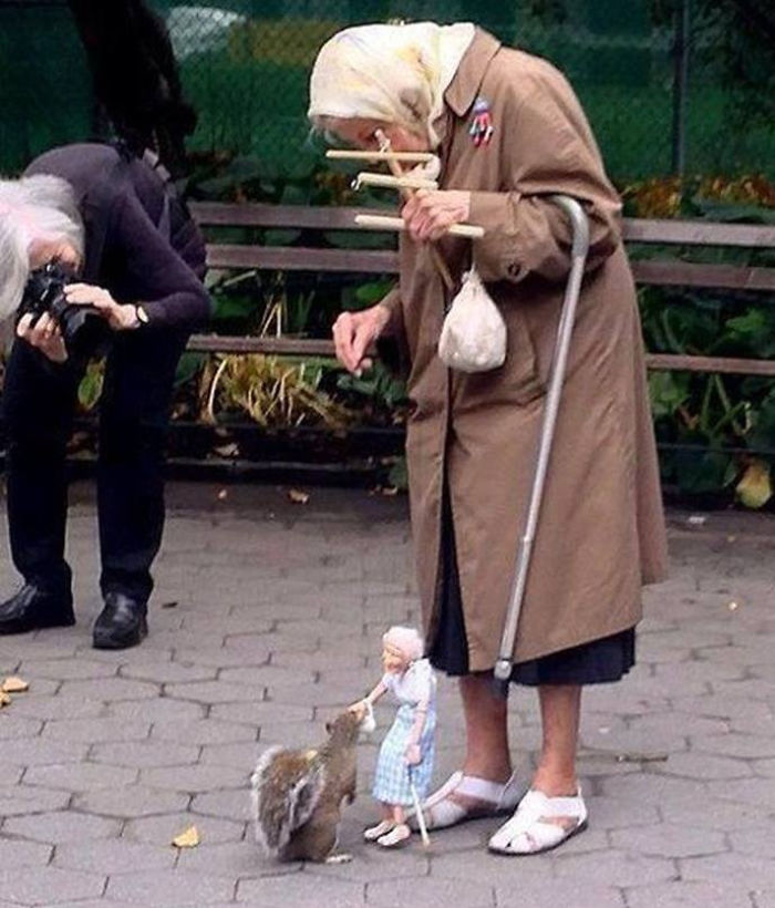 Old Woman Uses A Marionette Of Herself To Feed Squirrels In The Park