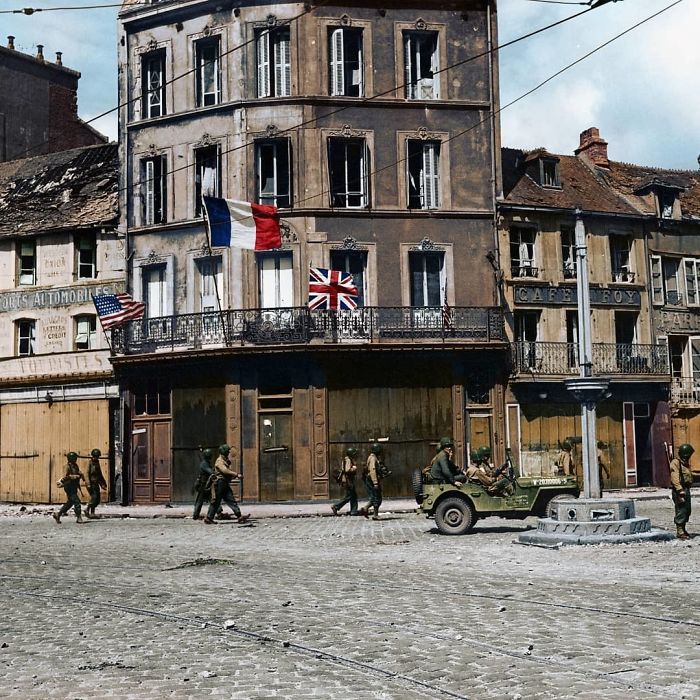 French Village With Storefronts, Soldiers Walking And Driving By