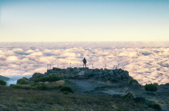 Panoramic view from a high vantage point in Madeira with a lone person overlooking clouds and landscape below.
