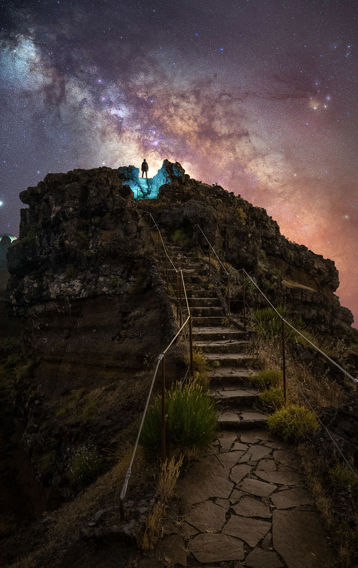 Person standing on rocky hilltop under a starry night sky in Madeira, showcasing magical nighttime adventure and scenic views.