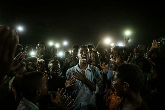 A Young Man, Illuminated By Mobile Phones, Recites A Poem While Protestors Chant Slogans Calling For Civilian Rule, During A Blackout In Khartoum, Sudan