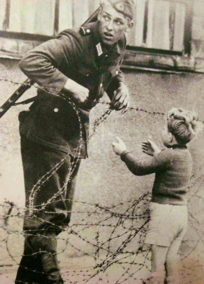 Soldado alemán desobedeciendo órdenes directas para ayudar a un niño a cruzar el recién formado muro de Berlín tras ser separado de su familia, 1961