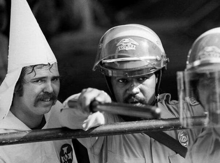 Miembro del Ku Klux Klan se esconde tras un policía para que le proteja, después de que una turba rodeara al Klan en Texas, 1983