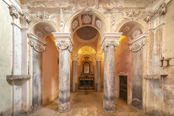 Interior view of an abandoned church in Europe featuring decorative columns and a historic altar in soft natural light.