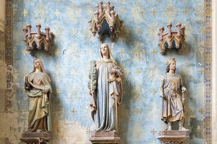 Statues of saints inside an abandoned church featuring detailed wall decorations and Gothic architectural elements.