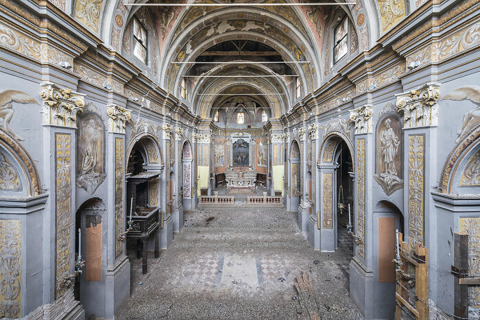 Interior view of an abandoned church in Europe showcasing ornate arches and faded religious frescoes and statues.
