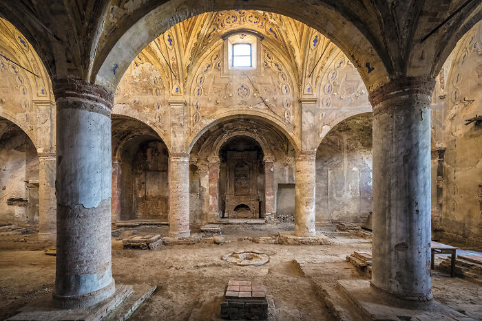 Interior of an abandoned church in Europe featuring old pillars, arches, and faded frescoes discovered during extensive travels.