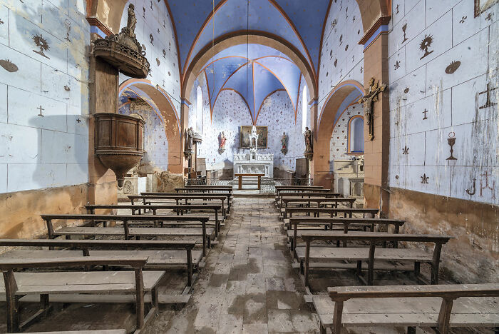 Interior of an abandoned European church with wooden benches and a blue ceiling showcasing historic religious architecture.