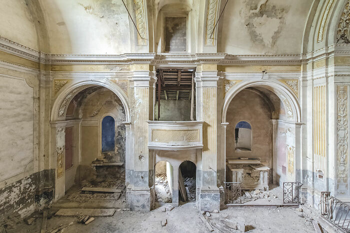 Interior of an abandoned church in Europe showing decayed walls, arches, and scattered debris in a historic religious building.