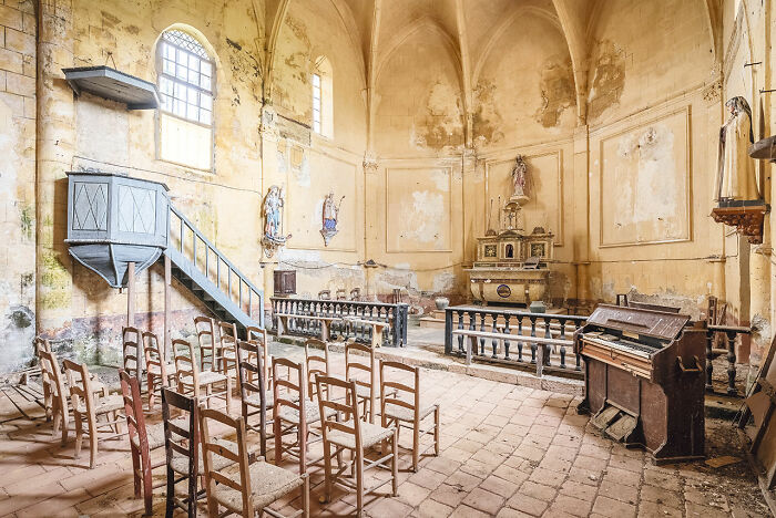 Abandoned church interior in Europe with worn walls, wooden chairs, old piano, and altar in a historic setting.