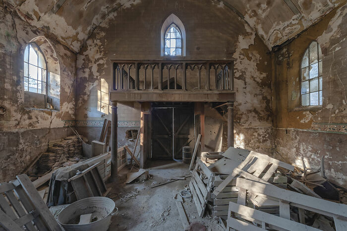 Interior of an abandoned church in Europe with decayed walls, broken furniture, and sunlight streaming through stained glass windows.