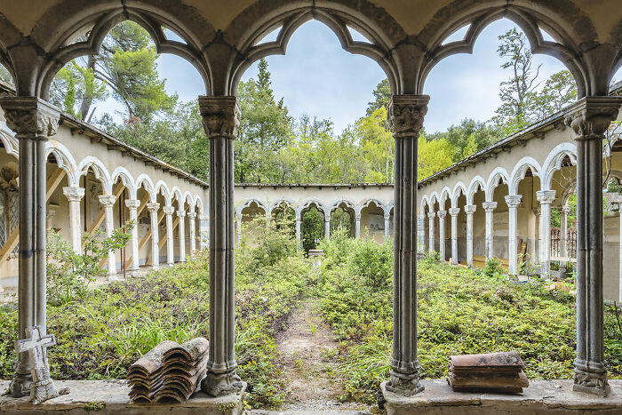 Abandoned European church courtyard overgrown with plants, featuring weathered stone arches and historic architecture.