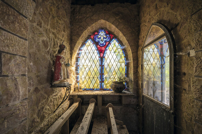 Abandoned church interior with stained glass window, stone walls, wooden pews, and a statue, discovered during Europe travels.