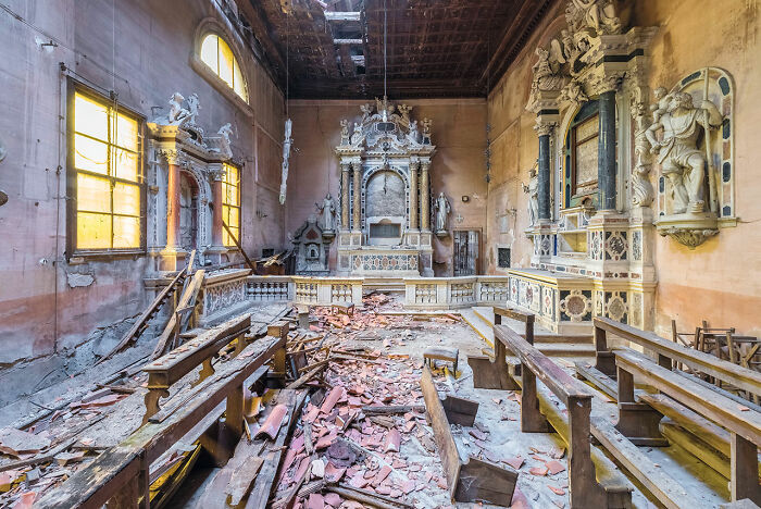 Interior of an abandoned church in Europe with broken benches, debris on the floor, and ornate, decaying decorations.