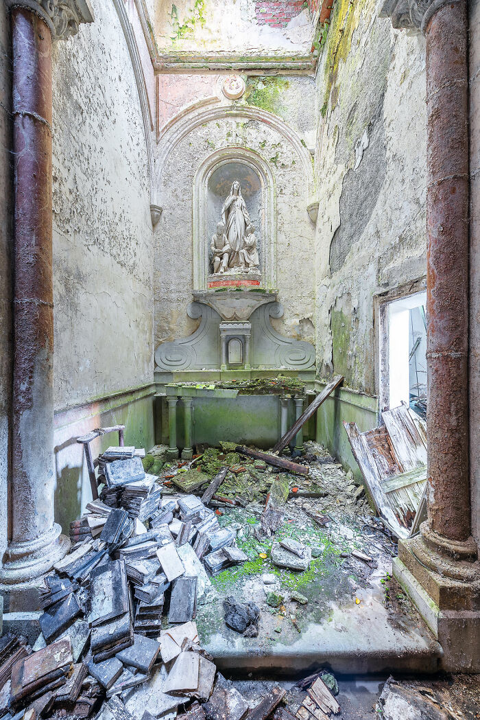 Interior of an abandoned church in Europe with peeling walls, rubble, and a religious statue above the altar in decay.