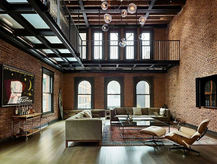 Living Area With Lots Of Exposed Brick Sits Beneath A Metal Catwalk In This Loft In New York City