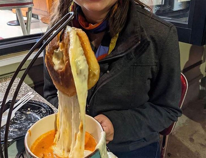 Bagel relleno de queso colgando sobre un bol de sopa de tomate
