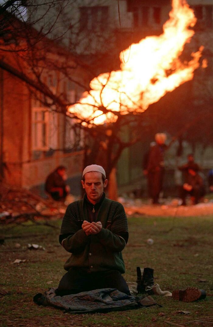A Chechen Man Prays During The First Battle Of Grozny, January 1995. The Flame In The Background Is Coming From A Gas Pipeline Which Was Hit By Shrapnel