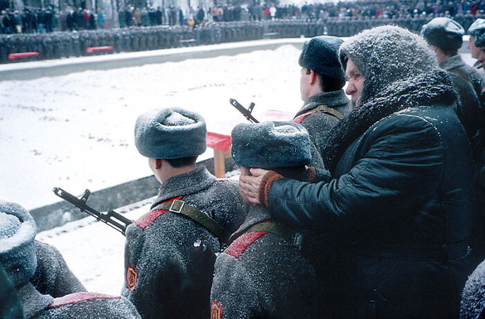 Una babushka mantiene calientes los oídos de su nieto, mientras él toma el juramento para enlistarse en el ejército ruso. Volgogrado, 1994. Foto de Nikolai Ignatiev