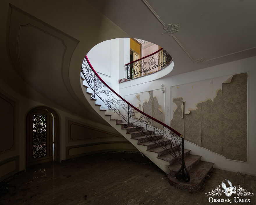 The Spiral Staircase Inside This Abandoned House Is Quite Unusual. It Has A Red Velvet-Covered Handrail, The Metal Work Depicts Dogs Running