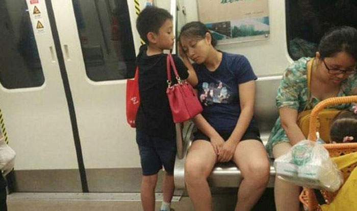 This Little Boy Gave Up His Seat To A Lady Who Entered The Train With A Stroller & Baby. Then As He Is Standing, His Mom Falls Asleep With Her Head On The Bare Railing