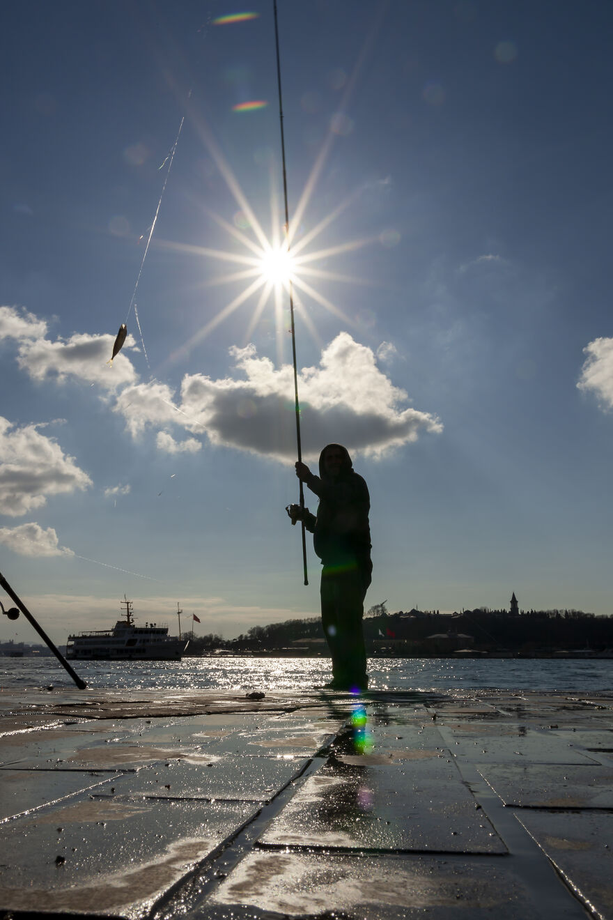 Fisherman On The Karakoy Port. In The Backdrop, One Can See The Old City With Topkapi Palace. The Sun Looks Like A Star, Why? The Aperture Is Low So Less Light Is Allowed In The Camera Thus Resulting In The Star Shape Of The Sun