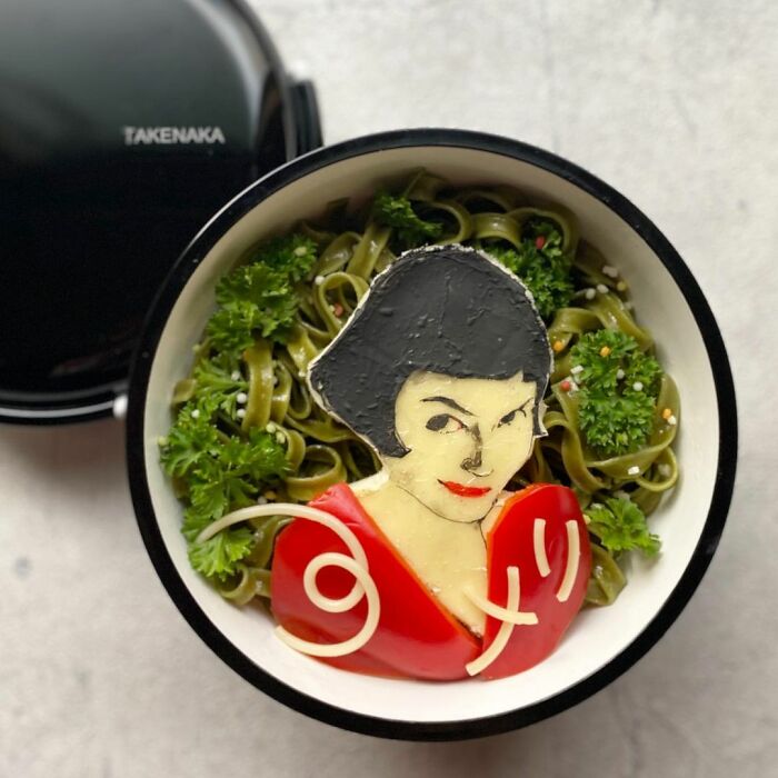 Bento artist crafts detailed lunchbox featuring a character with black hair and red outfit over green noodles and parsley.