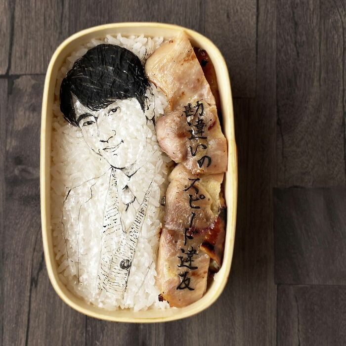 Bento art lunchbox featuring a detailed portrait rice design and grilled meat, inspired by favorite TV shows and manga.