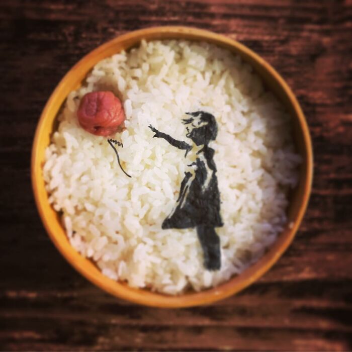 Bento artist creates detailed lunchbox art of favorite TV shows and manga, featuring rice with a seaweed silhouette design.