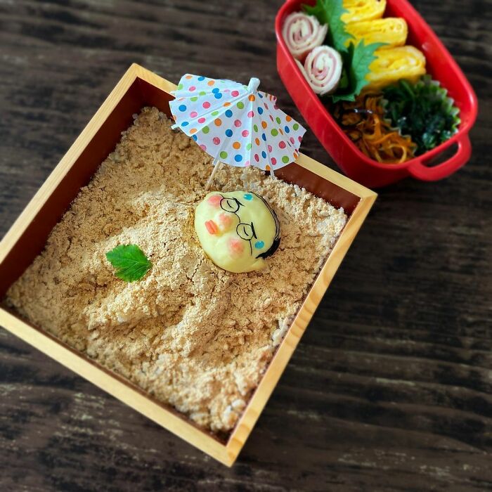 Bento artist creates detailed lunchbox with character design buried in textured food and colorful side dishes.