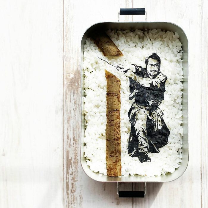 Bento artist creates detailed lunchbox art of a samurai character on a bed of rice using food ingredients.