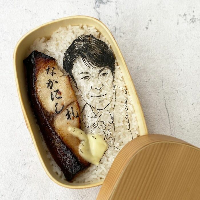 Bento artist creates detailed lunchbox with rice and fish, featuring a hand-drawn portrait on seaweed for her husband.