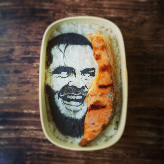 Bento artist creates detailed lunchbox art of a TV show character using rice, seaweed, and grilled salmon slice.