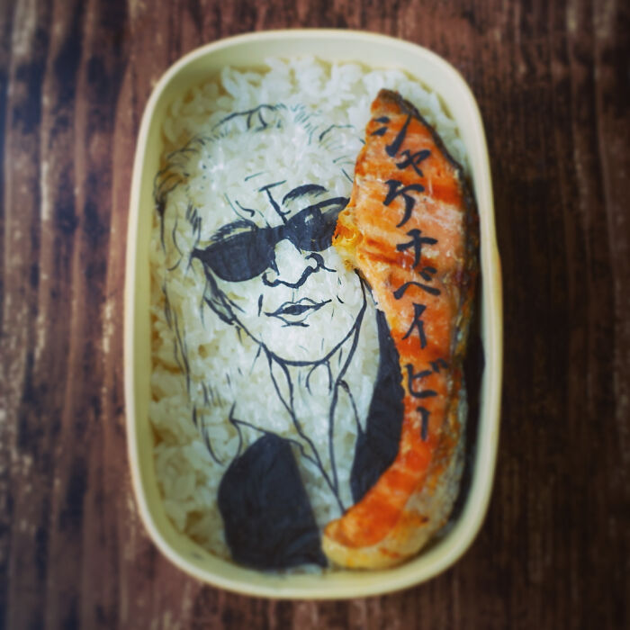 Bento artist creates detailed lunchbox featuring a character with sunglasses on rice beside a piece of grilled salmon.