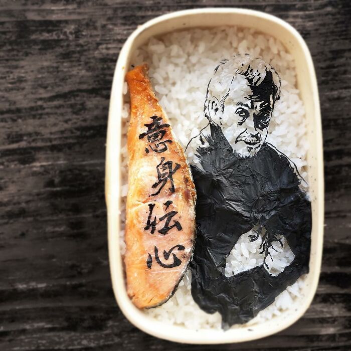 Bento artist's detailed lunchbox featuring a character made from seaweed and grilled fish with Japanese calligraphy on rice.