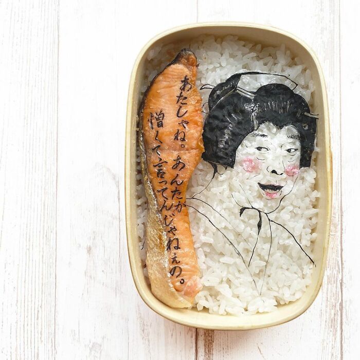 Bento artist creates detailed lunchbox featuring character illustration and Japanese text on rice with salmon slice.