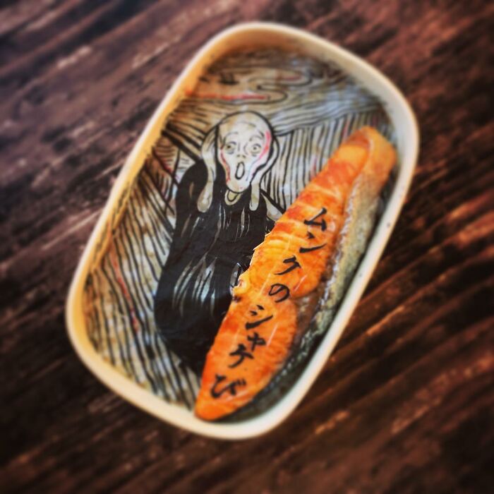 Bento artist creates a lunchbox featuring a detailed The Scream design with a salmon piece decorated with Japanese text.