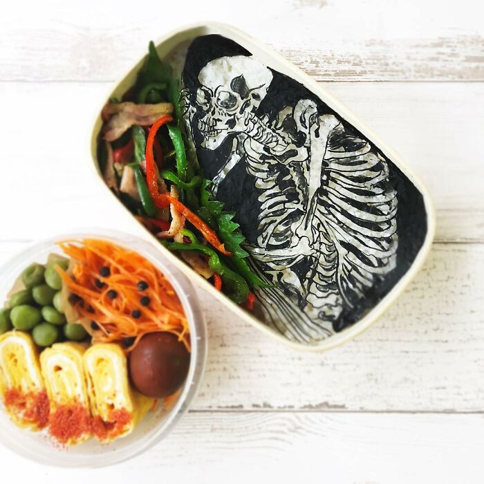 Bento artist lunchbox featuring detailed skeleton art with colorful vegetables and side dishes in a creative meal presentation.