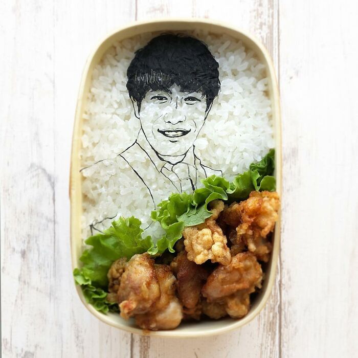 Bento artist lunchbox featuring detailed rice portrait and fried chicken with lettuce for a creative meal presentation.