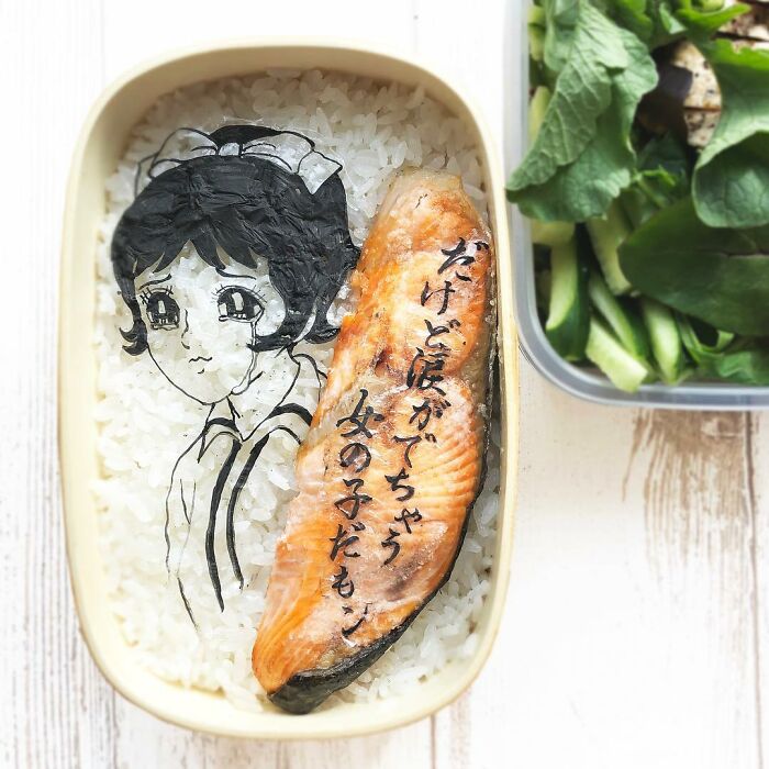 Bento artist lunchbox featuring detailed manga character art on rice with grilled fish and Japanese text design.