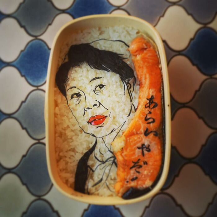 Bento art lunchbox featuring a detailed portrait on rice with a salmon piece and Japanese characters on the side.
