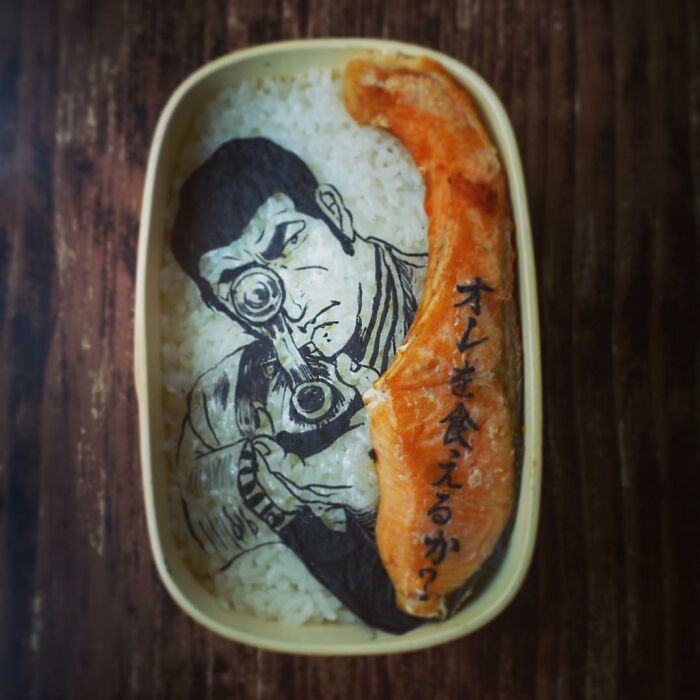 Bento artist’s lunchbox featuring detailed manga character art with rice and grilled salmon on a wooden surface