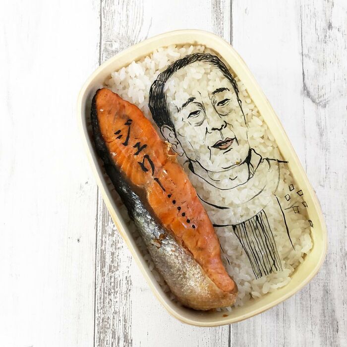Bento lunchbox featuring detailed rice art portrait and grilled salmon, showcasing creative bento artist’s work for her husband.
