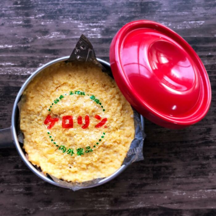 Close-up of a bento lunchbox with a textured omelet and decorative Japanese text, showcasing creative bento art.