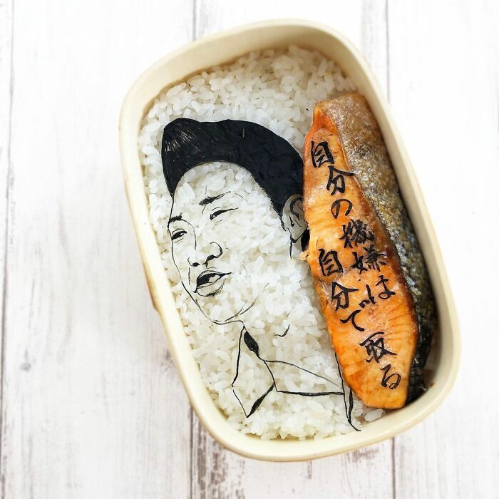Bento artist creates creative lunchbox featuring a detailed portrait and Japanese calligraphy on salmon and rice.