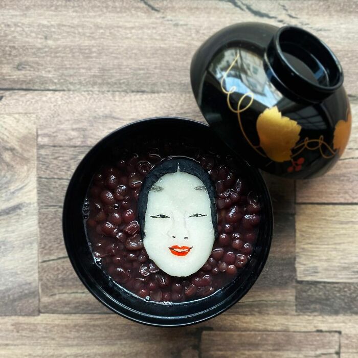 Bento artist creates a detailed face design with rice and seaweed in a traditional lunchbox filled with red beans.