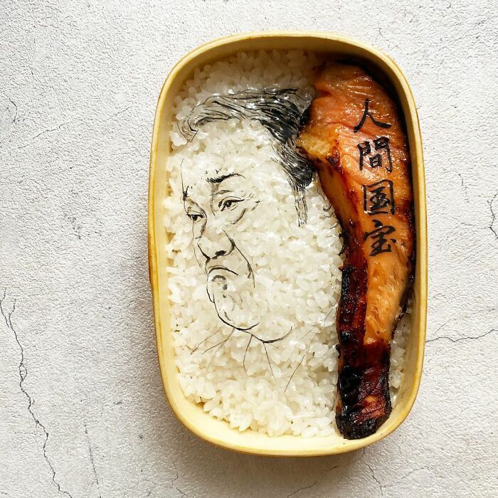 Bento artist lunchbox featuring rice with a detailed face drawing and grilled meat, inspired by favorite TV shows and movies.