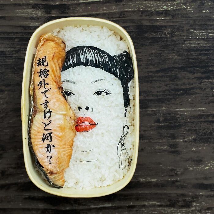 Bento artist lunchbox featuring detailed face art on rice with a piece of salmon and Japanese text on top.